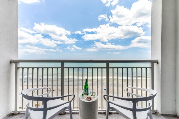 Relax on the private balcony with stunning ocean views, stylish seating, and a touch of luxury—complete with sparkling water, lime-garnished glasses, and light snacks for the perfect getaway vibe.