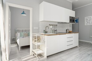 Compact open-plan kitchen with white cabinets and a sleeping area just behind, combining functionality with style.

