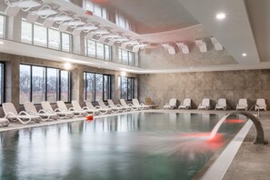 Luxurious indoor swimming pool with elegant loungers and large windows for a relaxing atmosphere.