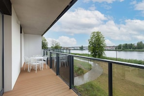 Modern balcony with outdoor seating and a scenic view of lush greenery and water.