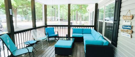 Screened in porch with plenty of seating, a fan, & strip lights for night.