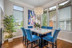 Adjacent counter height dining room table and chairs adorned with a chandelier and windows for natural light.  Make sure you take a picture with Freddie Mercury.