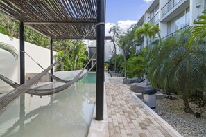 Hammock lounge over water, surrounded by greenery and a shared pool.