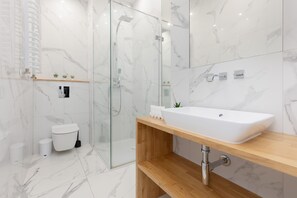 A contemporary bathroom with a walk-in shower, marble-style tiling, and a minimalist sink and vanity setup.