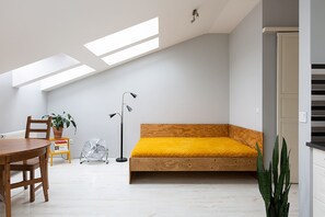 Modern studio apartment featuring a yellow sofa bed and large skylights for ample natural light.

