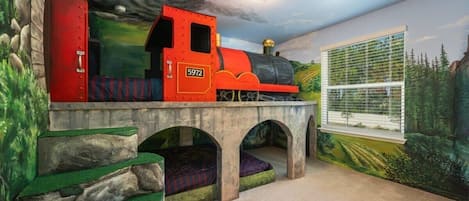 All aboard the adventure express! This train-themed room offers a magical escape for kids with bunk beds and scenic murals.