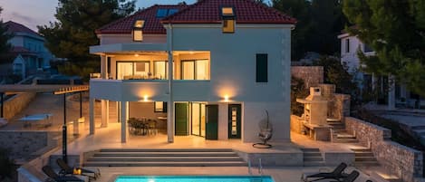 View of Croatia luxury family villa with private pool surrounded by deckchairs and outdoor grill