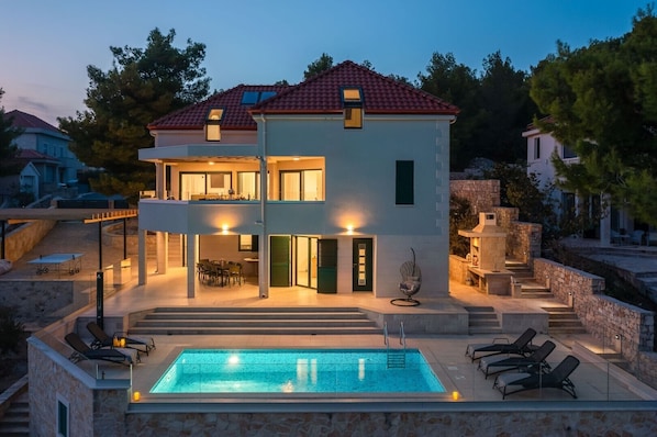 View of Croatia luxury family villa with private pool surrounded by deckchairs and outdoor grill