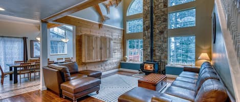 Come experience our spacious living room! Sink into the plush leather couch in our airy sanctuary, embraced by stunning vaulted ceilings and a rustic stone wall. Let the warmth of the wood stove envelop you in comfort.