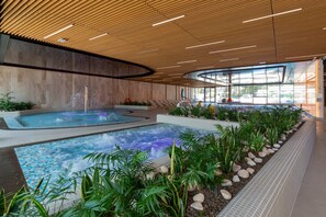 Indoor pool zone accented by wooden ceilings and vibrant plants, offering a serene spa experience.

