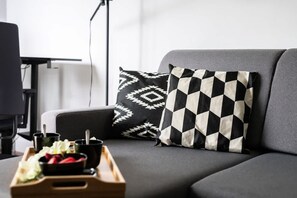 Close-up of a comfortable grey sofa with decorative pillows and a tray with refreshments.

