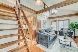 View of living room, the stairs which lead to the loft, and the door leading to the riverside deck.