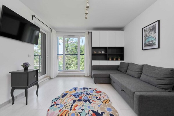 Modern living room with a comfortable grey sofa, colorful rug, and an open-plan kitchen.

