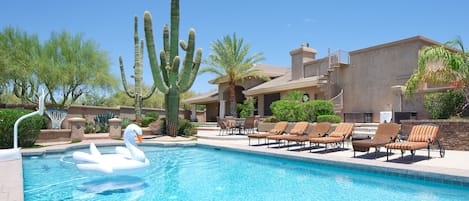 Resort-Style backyard featuring a large sparkling blue heated pool with a basketball hoop for friendly competitions in the water and sun loungers for basking in the valley of the sun!