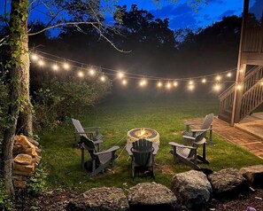 Sweet firepit with 5 Adirondack chairs and string lights for the perfect outdoor cookout or hang out location.