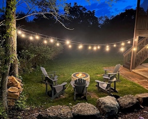 Sweet firepit with 5 Adirondack chairs and string lights for the perfect outdoor cookout or hang out location.