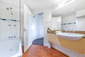 A spacious bathroom comes complete with a shower over a bathtub, a vanity and unique terracotta tiles