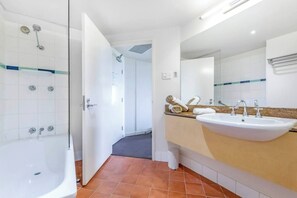 A spacious bathroom comes complete with a shower over a bathtub, a vanity and unique terracotta tiles.