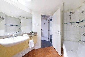 A spacious bathroom comes complete with a shower over a bathtub, a vanity and unique terracotta tiles.
