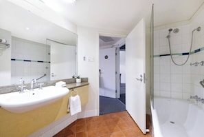 A spacious bathroom comes complete with a shower over a bathtub, a vanity and unique terracotta tiles.