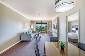 A naturally-lit living room has a large, L-shaped couch, coffee table and a wall-mounted, flat-screen TV with Foxtel.