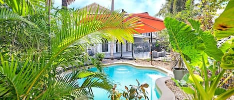 The private pool is surrounded by lush greenery, and sits under a large shade umbrella. 
