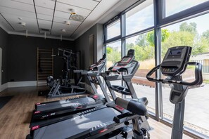 Well-equipped gym with cardio machines and large windows offering natural light.

