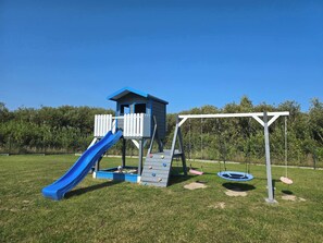 Outdoor playground featuring a slide and swing set surrounded by an open grassy area.

