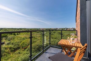 Balcony with a wooden table and chairs offering scenic views of lush greenery.

