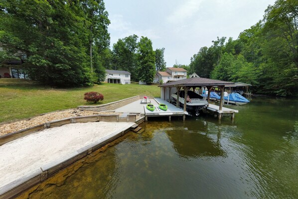 Beach, dock and waterfront view from water with cottage in background.