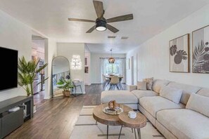 Beautiful Living Room w/ Smart TV, Large Sofa, Reading Material, Full Body Mirror, Fun Light Up Decor, Room Darkening Shades, & Ceiling Fan & Lighting