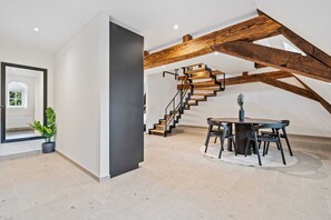 Dine in style in our elegant dining area, featuring a modern table set under stunning exposed beams and a unique staircase design.