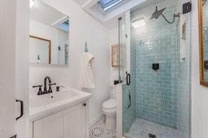 The bathroom features a rainfall shower with updated coastal tile. Essential toiletries are provided
