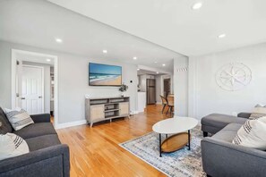 Spacious living room with smart TV, sectional couch, standard couch, and hightop table for added workspace or dining