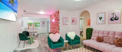 Pink living rom (accented by green chairs) with tv and cool hanging displays