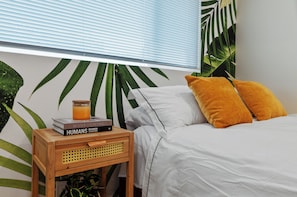 Cozy bed nook w/ soft linens, comfy pillows, nightstand, books & scented candle.