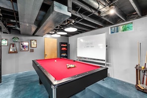 The basement is filled with exciting entertainment options, including a dart board, bar top table with chairs, pool table, mini fridge, and board games.