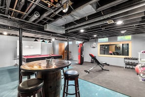 The basement is filled with exciting entertainment options, including a dart board, bar top table with chairs, pool table, mini fridge, and board games.