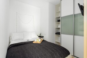 A cozy bedroom featuring a white bed, minimalist decor, and a wardrobe with frosted glass panels.

