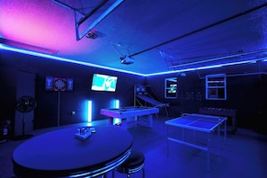 LED lit game room with 65" Tv, pool table, foosball table, ping pong table, basketball game, dart board, tick tack toe, and bar table