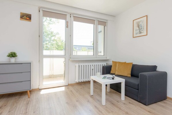 A bright living area with a gray sofa, a small coffee table, and large windows letting in natural light.

