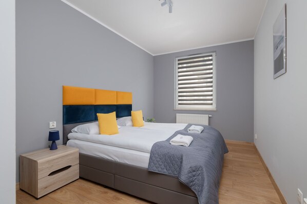A bright bedroom with a comfortable bed featuring a vibrant yellow and blue headboard and minimalistic decor.


