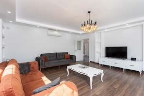 Open-plan living room with sofas, dining area, kitchen, A/C, WiFi internet, and satellite TV