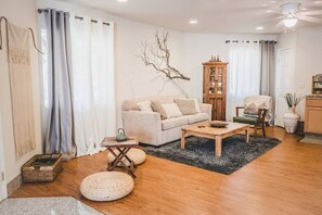 The serene living area features a high-quality sleeper sofa, double ceiling fans for ultimate comfort, a Japanese-inspired tea table, and a large coffee table that doubles as a "family style" dining table for parties of 3 or more.