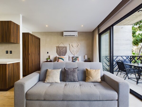 Cozy gray sofa, king bed with boho macramé, and a private balcony with natural light.