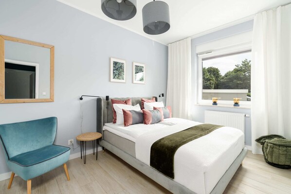 A cozy bedroom with a comfortable bed, green accents, and a seating area by the window for relaxation.

