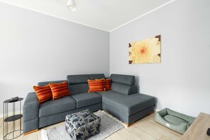 A living room with a modern gray sofa, vibrant orange cushions, and a stylish coffee table.

