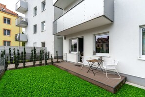 An outdoor view of a private garden with a small deck and seating area, surrounded by greenery.

