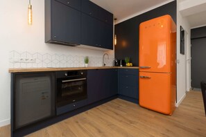 A modern kitchen featuring dark cabinets, a bold orange retro-style fridge, and sleek finishes.

