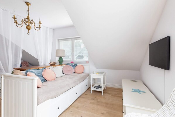 A cozy living area with a white daybed, soft pink accents, and an elegant chandelier.

